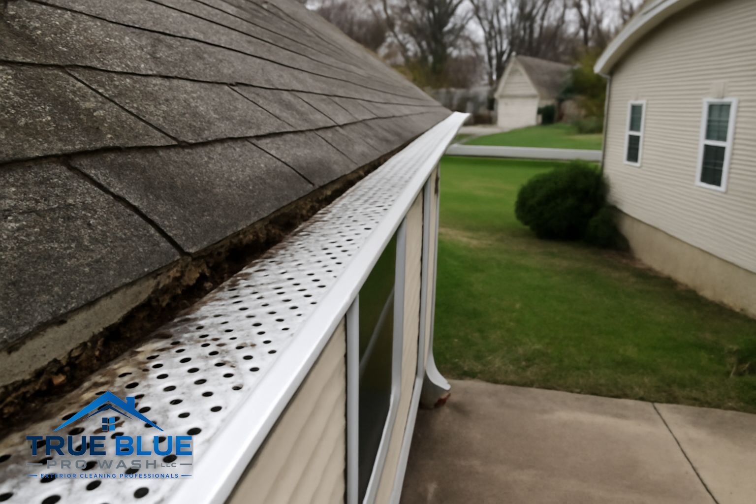 Technician clearing a clogged gutter on a Hockessin Delaware home surrounded by mature oak trees