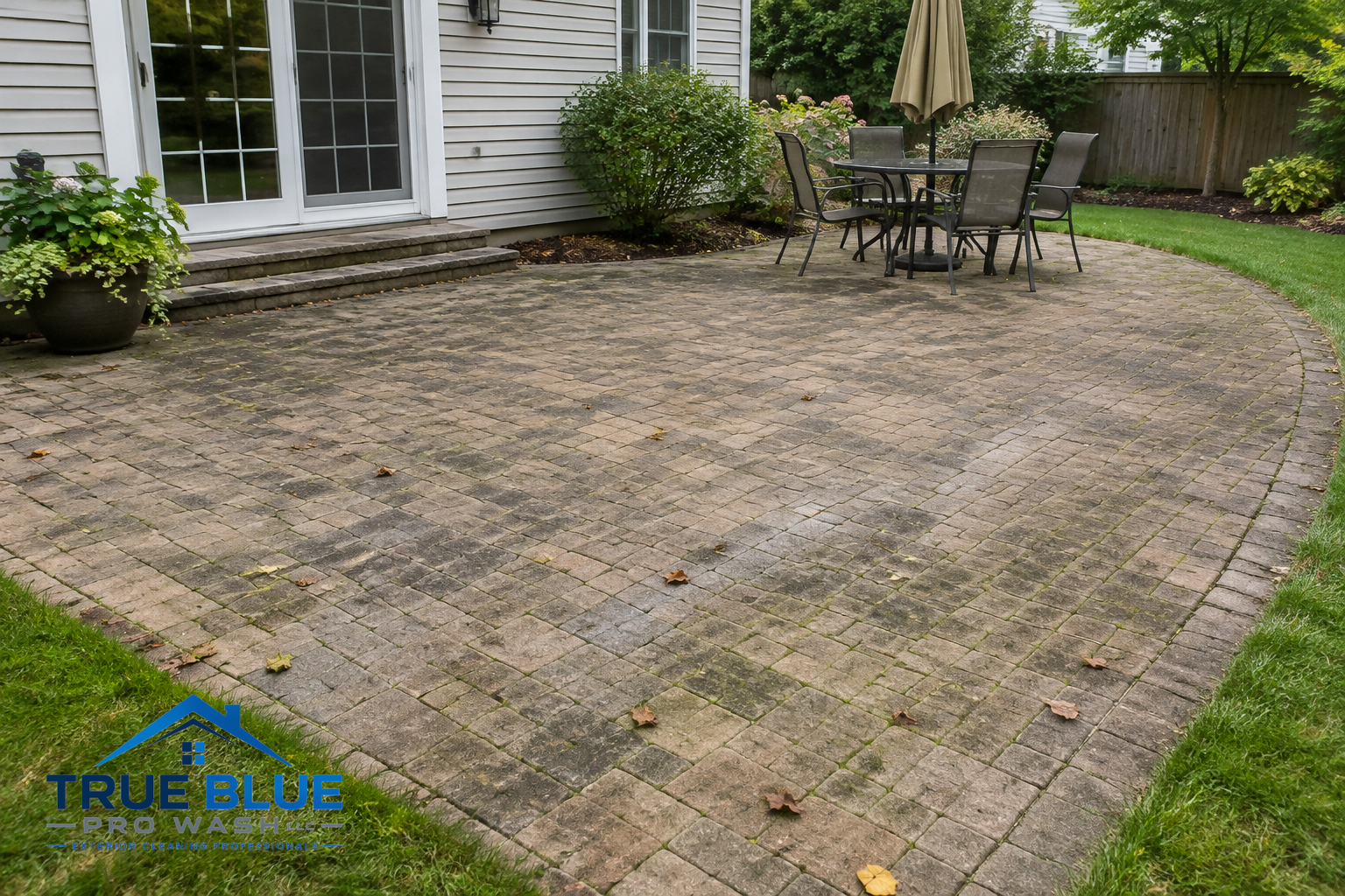 A backyard paver patio with dirt and leaves on its surface, needing cleaning.