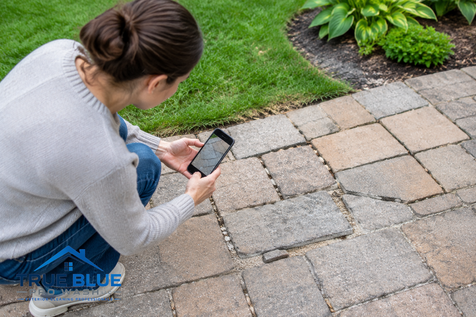 Homeowner photographing damaged paver patio areas with a phone for documentation.