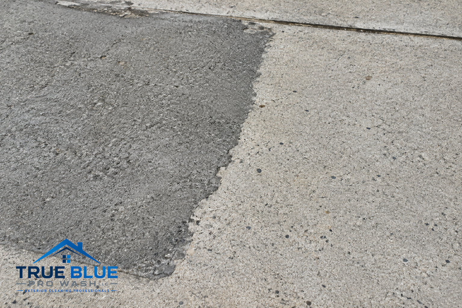 Close-up of concrete driveway surface showing boundary between darker repair patch and lighter original area.